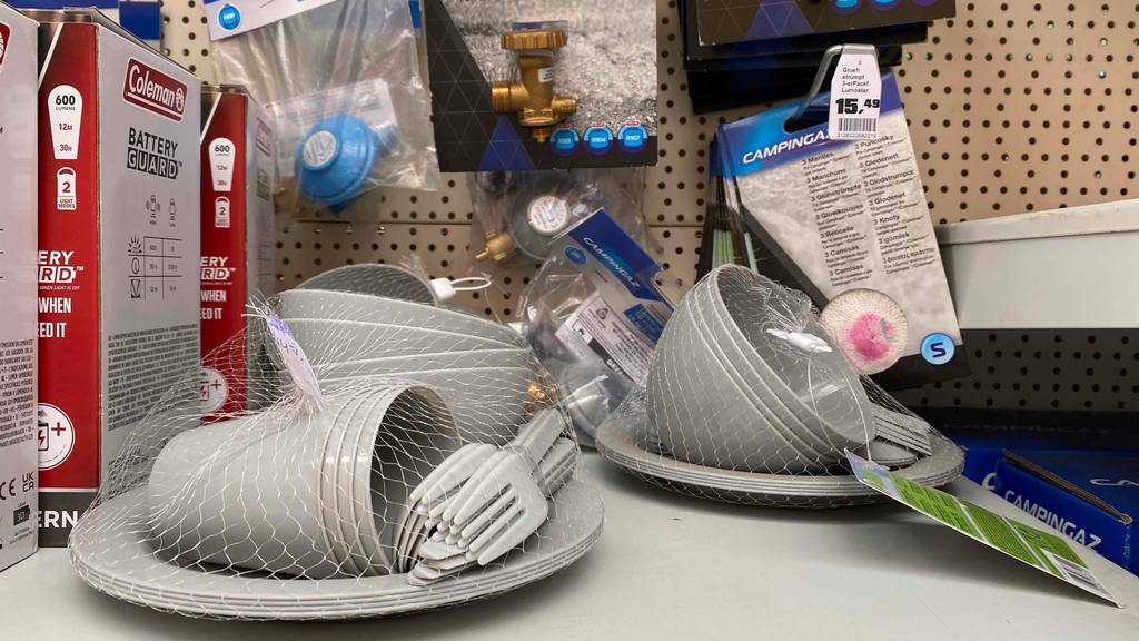 Campinggeschirr-Test: Campinggeschirr in einem Netz stehen in einem Regal neben anderen Produkten.