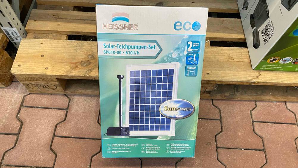 Im Test: Eine verpackte Solar-Teichpumpe lehnt an einer Holzpalette.