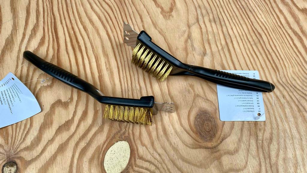 Zwei getestete Grillbürsten aus Messing liegen auf einem Holz mit Etikett darauf.
