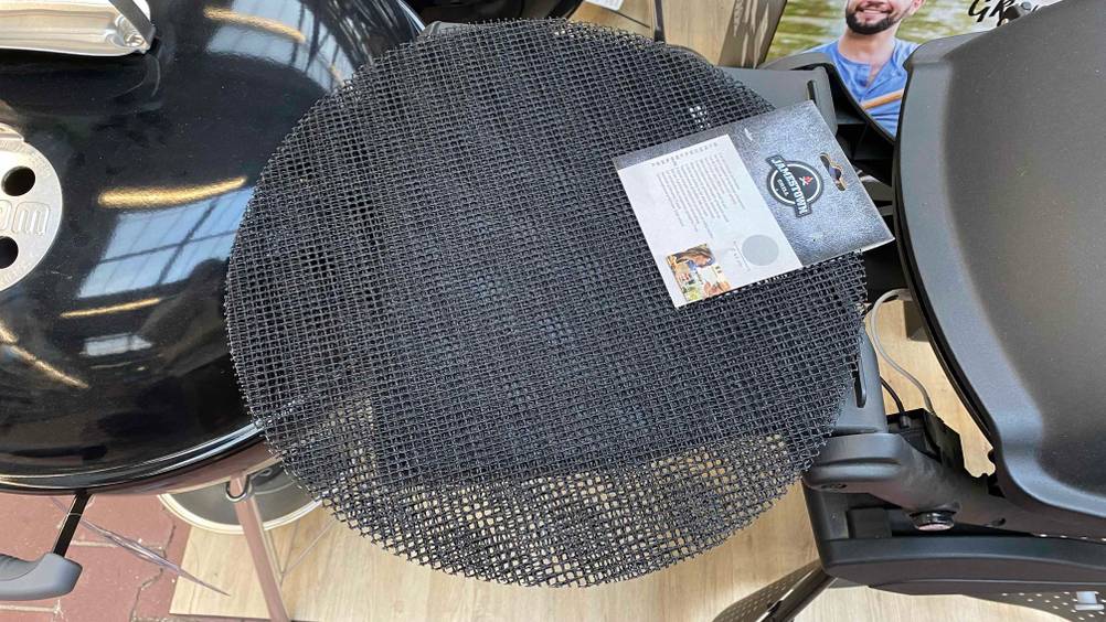 Grillmatte im Test: Eine schwarze Grillmatte ist neben einem Kugelgrill aufgelegt.