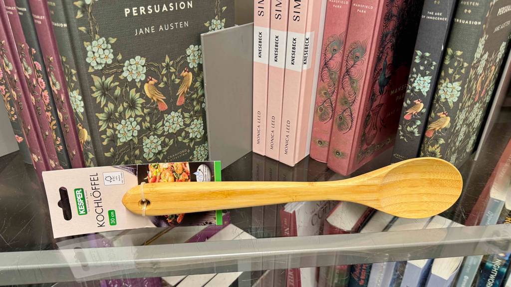 Test: Ein Holz-Kochlöffel liegt vor mehreren Büchern in einem Regal.