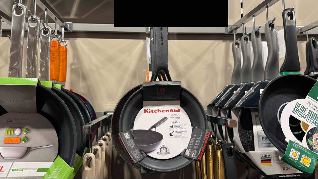 Die getestete KitchenAid-Pfanne hängt in einem Geschäft neben anderen Pfannen.