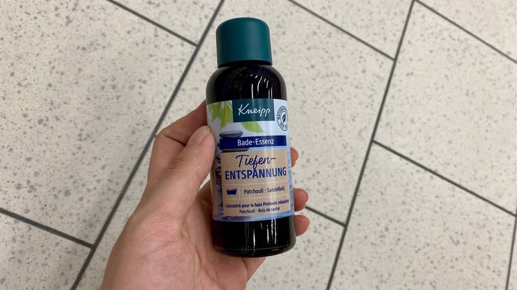 Badeöl getestet: Eine Hand hält eine Flasche Öl vor einen Fließenboden