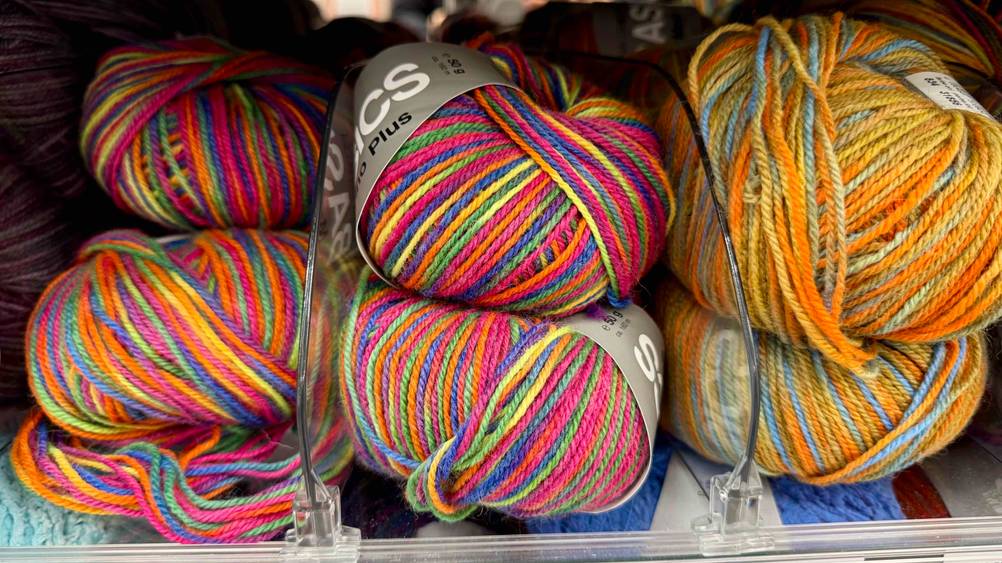 Die getestete Regenbogen-Wolle in verschiedenen Farben befindet sich in einem Regal neben anderen Wollen.