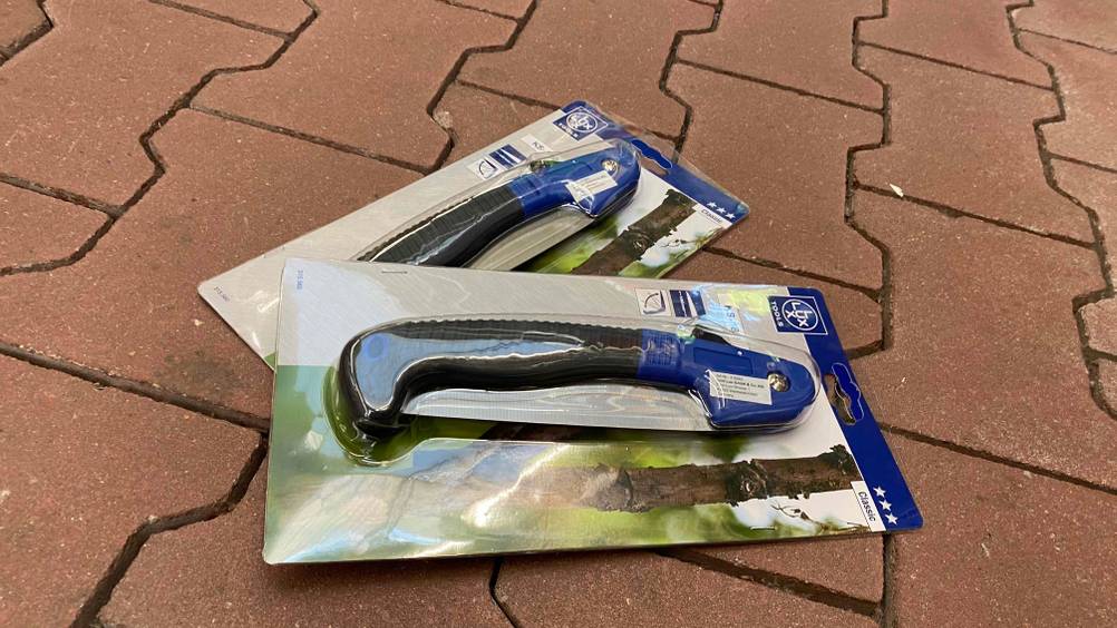 Klappsäge im Test: Zwei Klappsägen in Verpackung auf einem roten Steinboden.