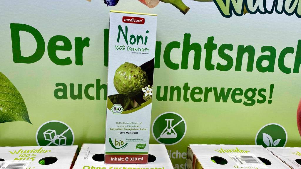 Noni-Saft getestet: die Verpackung eines Noni-Saftes vor einer Werbetafel.