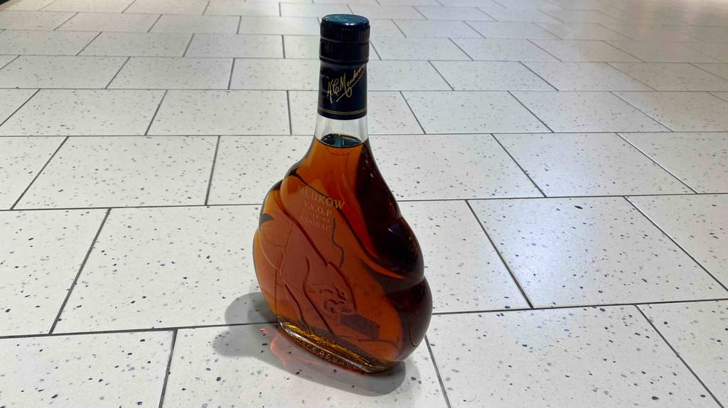 Eine getestete Flasche Cognac stehend auf einem Fliesenboden.