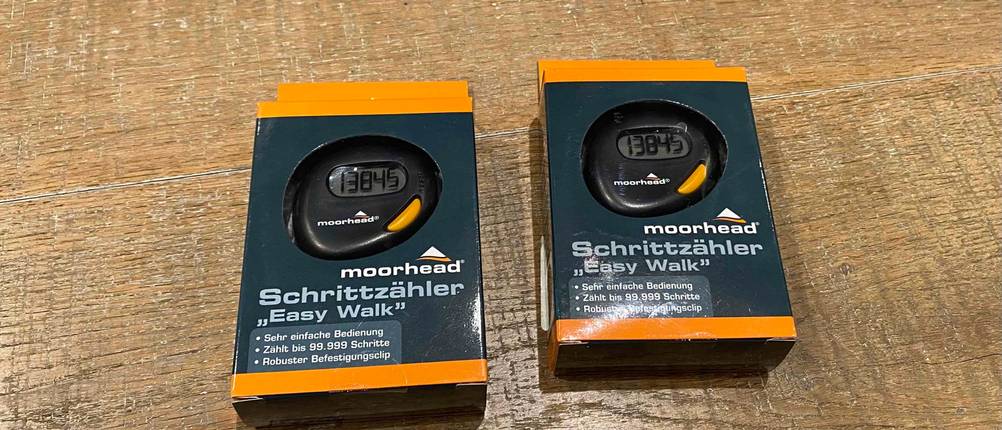 Schrittzähler im Test: 2 verpackte Schrittzähler liegen nebeneinander auf einer Holzfläche