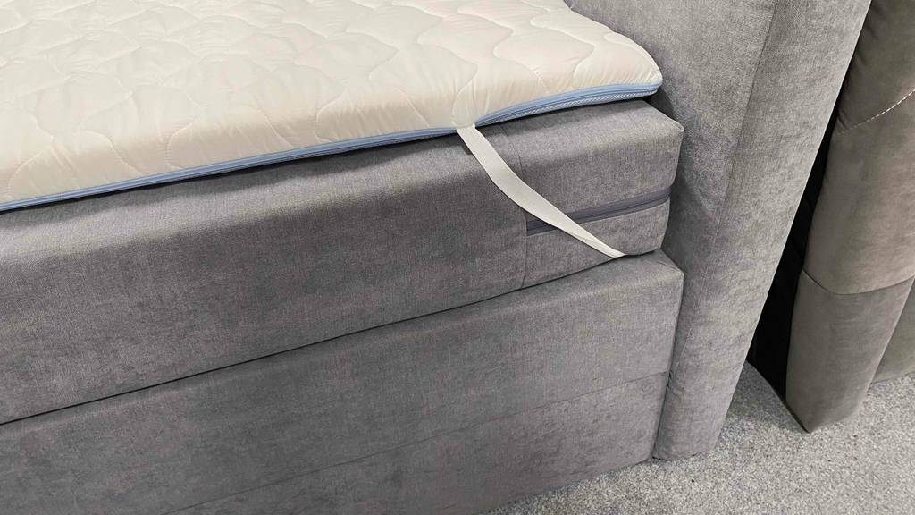 Boxspringbett-180x200 im Test: Bettrahmen und darauf ein Topper mit einem Gummiband.