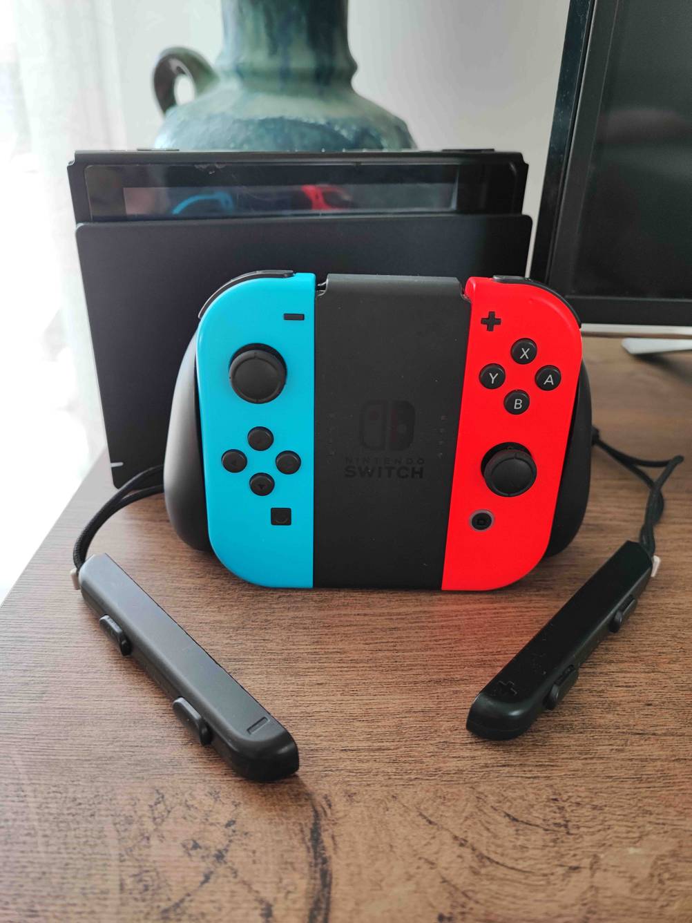 Getestete Handheld-Konsole mit Zubehör wie Ladestation und weiteren Kontrollern auf einem Holztisch stehend.