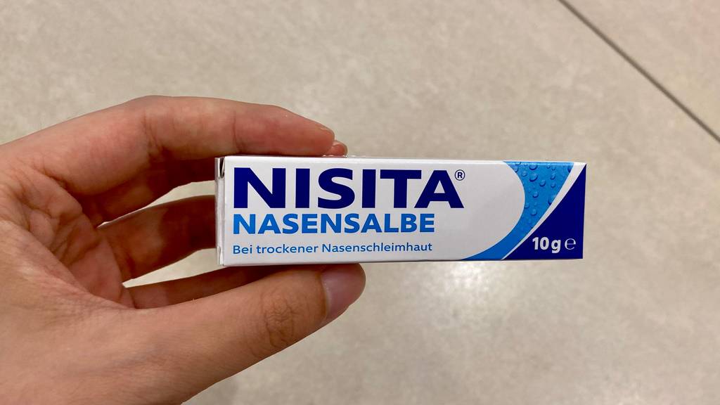 Nasensalben im Test: Eine Hand hält eine Packung Salbe vor einen hellen Hintergrund