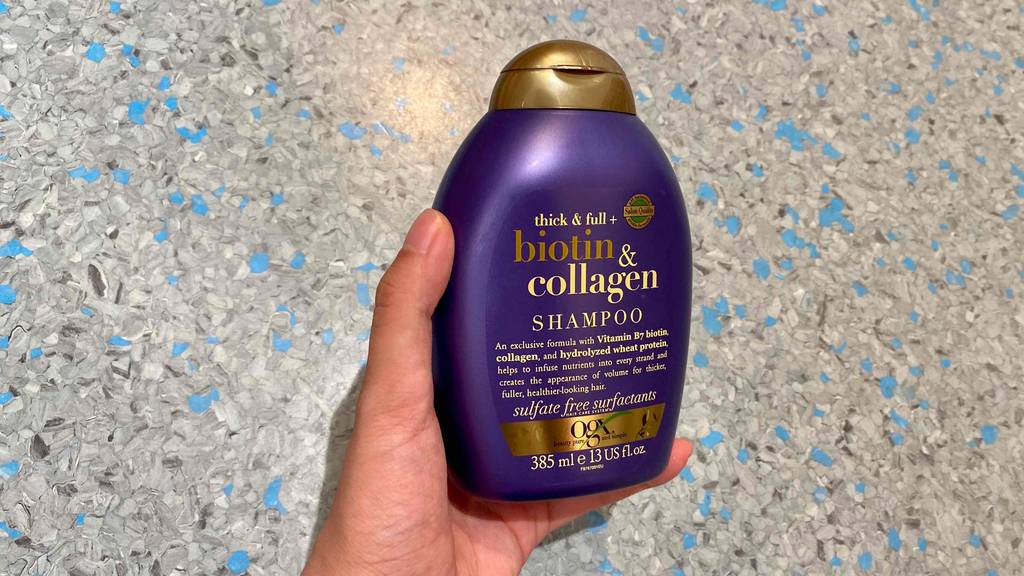 OGX-Shampoo im Test: Eine Hand hält eine Flasche Shampoo vor Fließenboden
