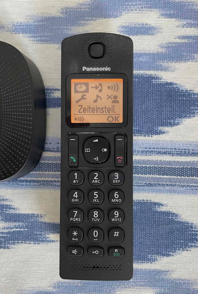 Vorderansicht eines getesteten schnurlosen Telefons von Panasonic auf blau-weiß-gemustertem Untergrund.