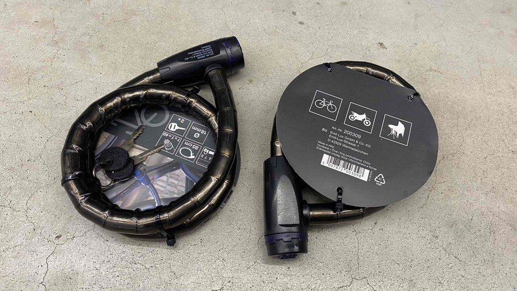 Fahrradschloss getestet: Zwei originalverpackte Schlösser eines mit der Rückseite nach oben auf einem Steinboden liegend