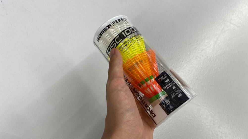 Badminton-Bälle im Test: Eine Hand hält eine Packung vor eine weiße Wand
