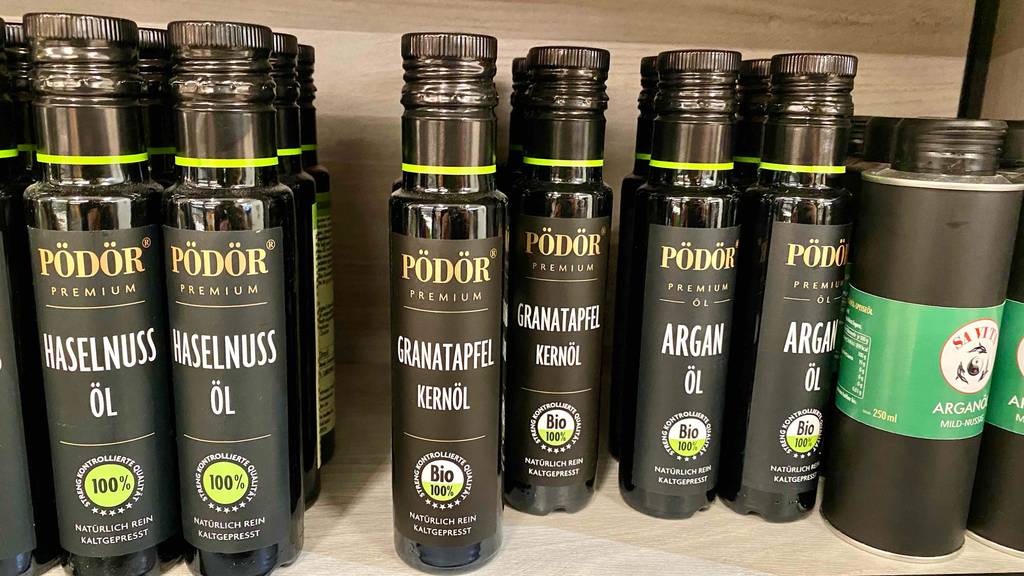 Mehrere Flaschen getestetes Granatapfelkernöl stehen neben anderen Produkten im Regal.