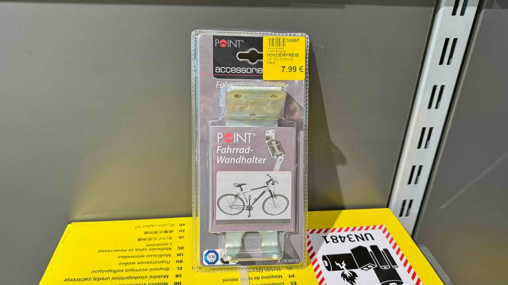 Die getestete Fahrrad-Wandhalterung lehnt an einr Regalwand in der Verpackung.
