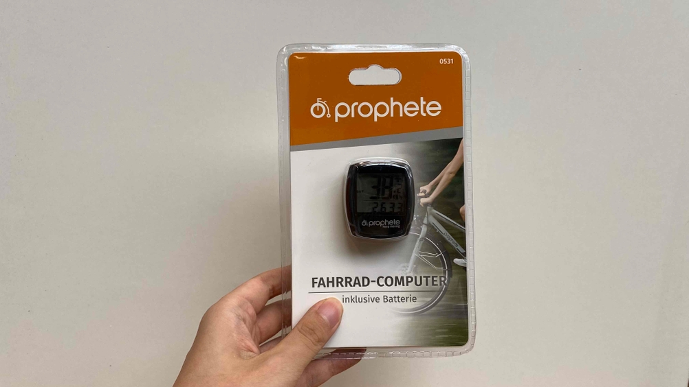 Fahrradcomputer im Test: Eine Hand hält ein origialverpacktes Gerät vor eine weiße Wand