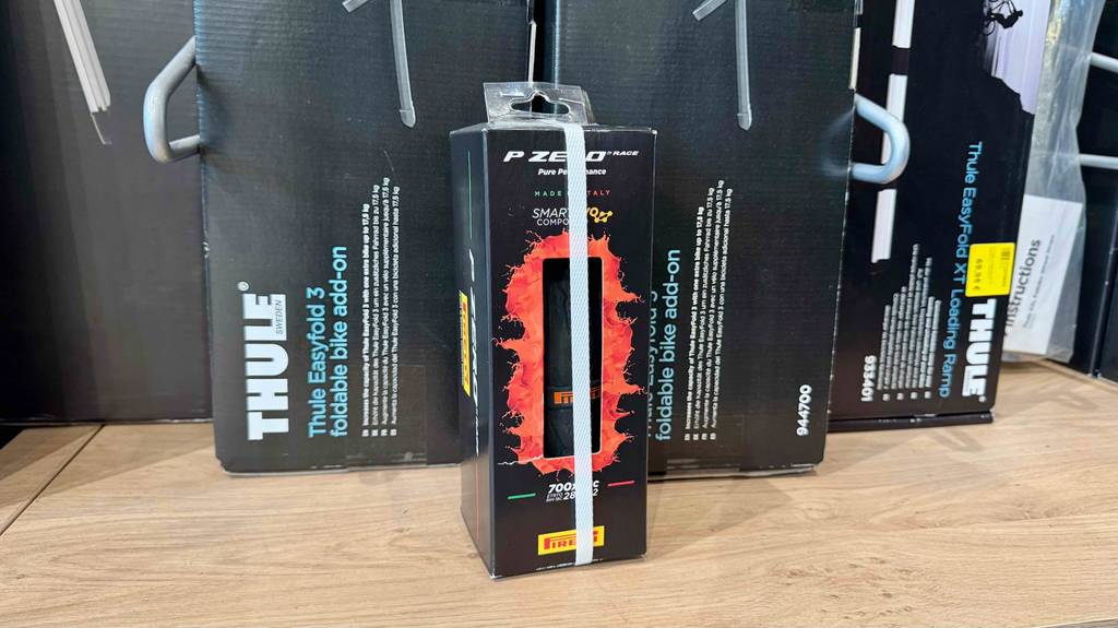 Eine Verpackung des getesteten Rennrad-Reifens (28-622) steht vor einem Regal mit Fahrradständern.