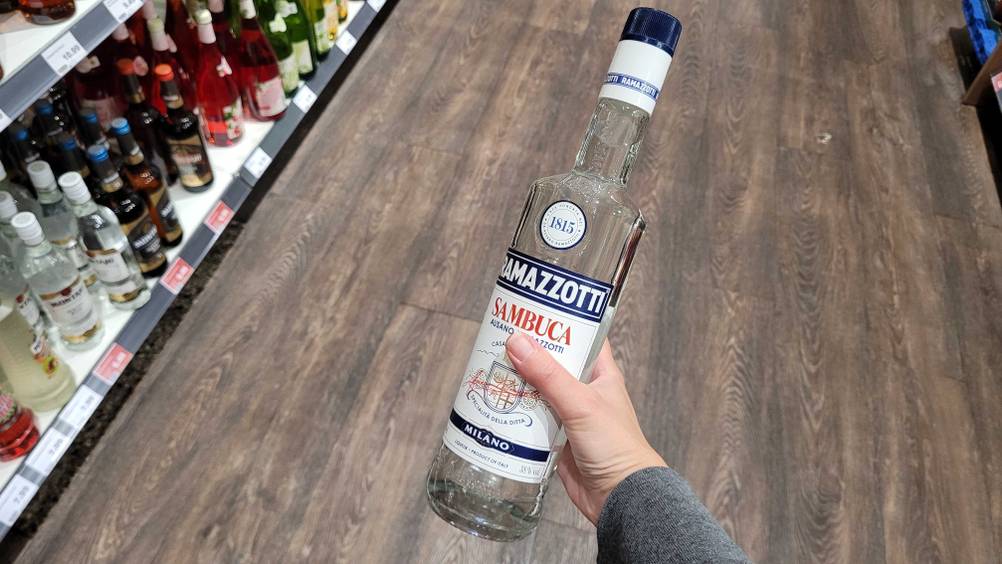 Im Test: Eine Hand hält eine Flasche Sambuca vor einen Holzboden