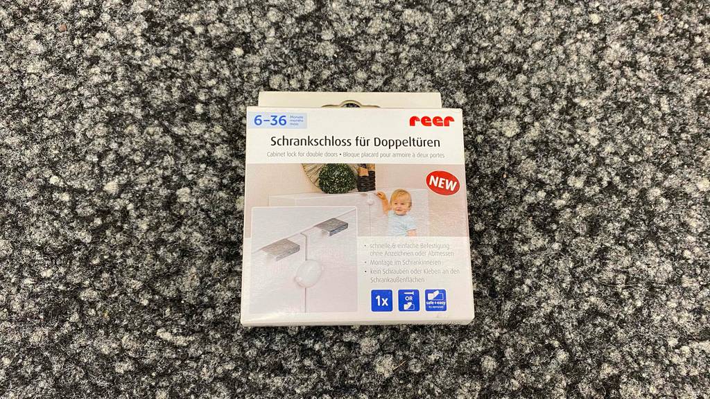 Schrank-Kindersicherung im Test: Auf einem grauen Teppich liegt eine Schrank-Kindersicherung.