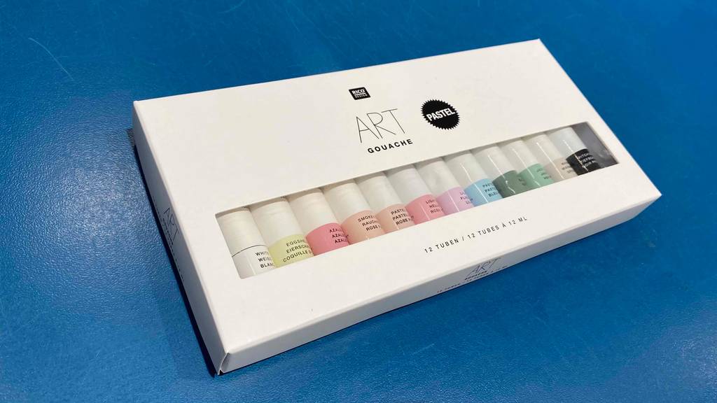 Im Test: Eine Packung Gouachefarben mit mehreren verschiedenfarbigen Tuben auf einem blauen Untergrund