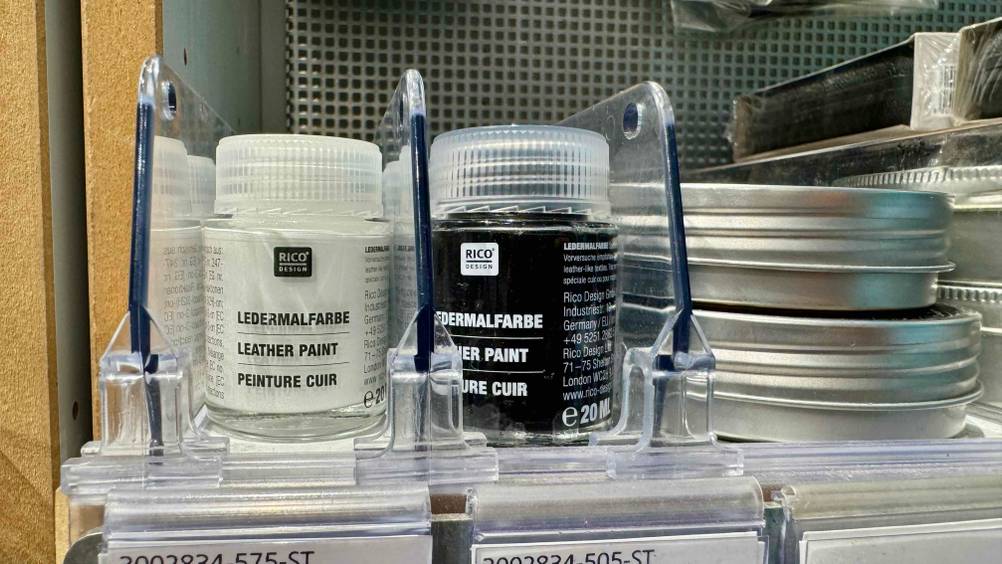 Die getestete Lederfarbe in Schwarz steht neben einer weißen Ledermalfarbe.
