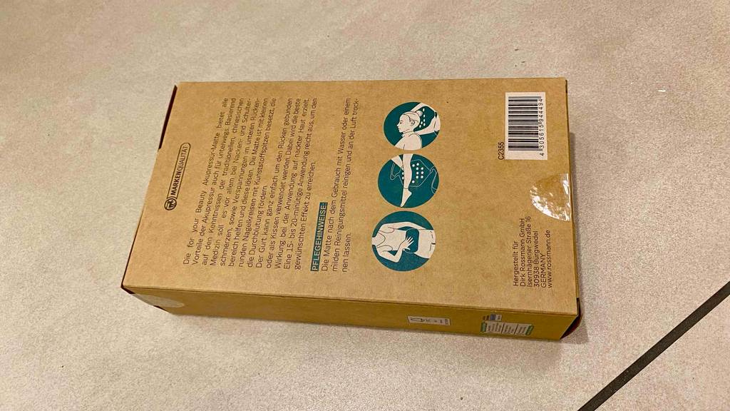 Akupressurmatte im Test: Rückseitee der Verpackung einer Akupressurmatte, die auf einem Boden patziert ist.