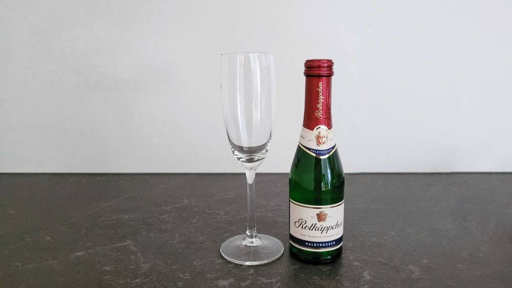 Eine Flasche getesteter Sekt neben einem Glas auf einer dunklen Fläche.