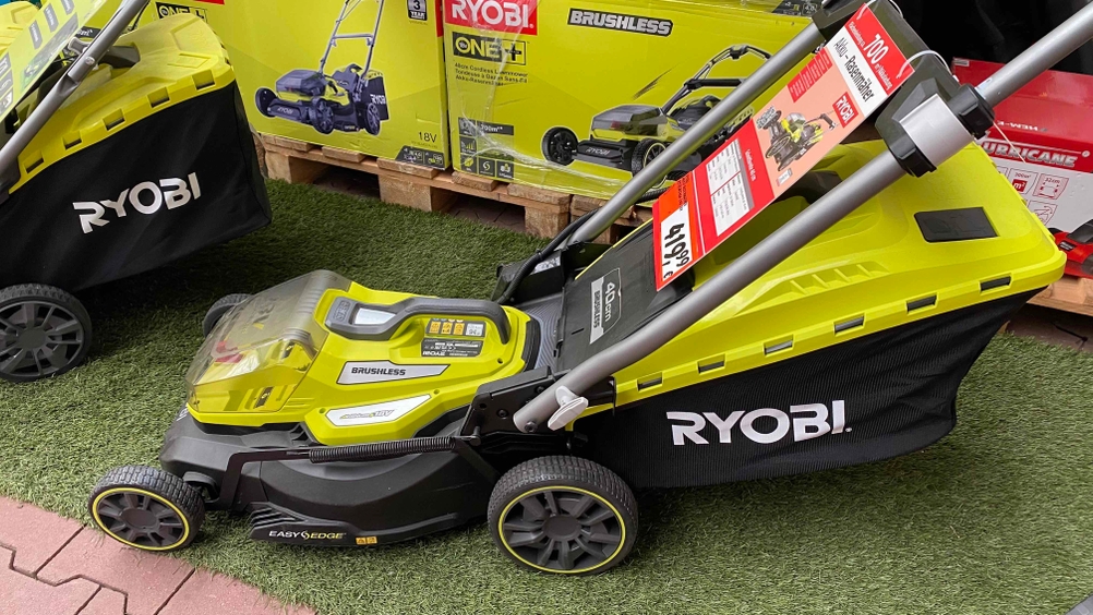 Akku-Rasenmäher im Test: gelber Akku-Rasenmäher von der Seite vor Verpackungen des Rasenmähers.