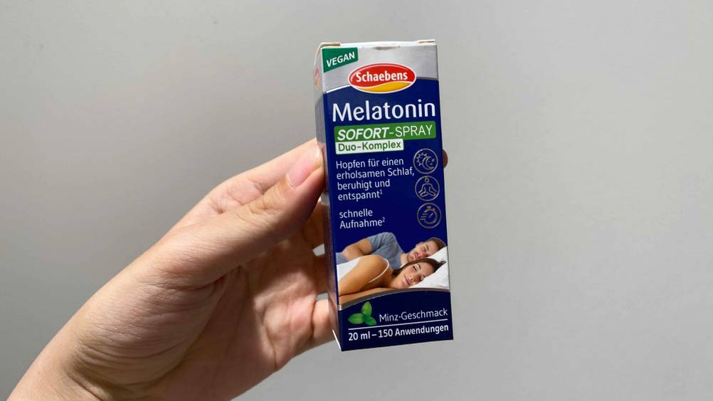 Melatonin-Spray getestet: Eine Hand hält eine Packung vor eine helle Wand