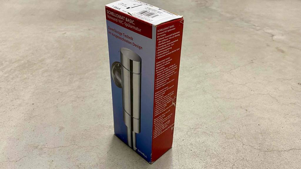 WC-Druckspüler im Test: eine Verpackung von WC-Spülarmatur schräg auf einem Boden stehend.
