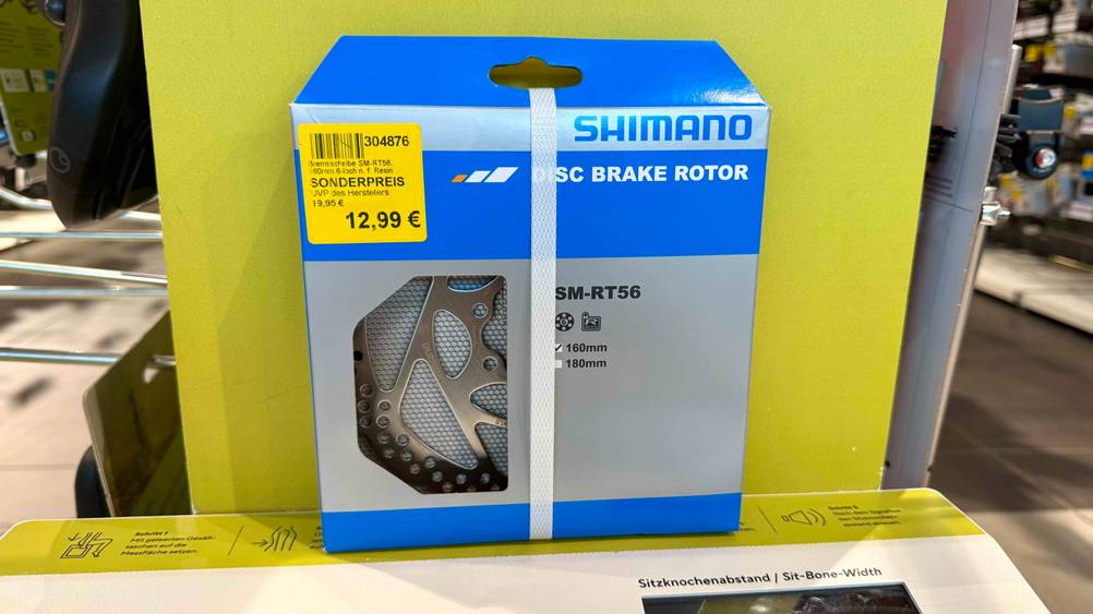 Die getestete Shimano-Bremsscheibe, mit Preisschild auf der Verpackung ist auf einen Karton gestellt.