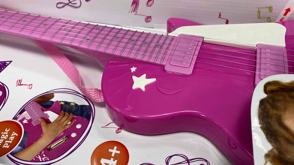 Kindergitarre-Test: Saiten-Detail der liegenden, rosa Gitarre im Karton.