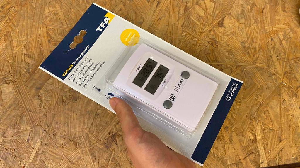 Hygrometer getestet: Eine Hand hält ein verpacktes Gerät vor eine Holzfläche