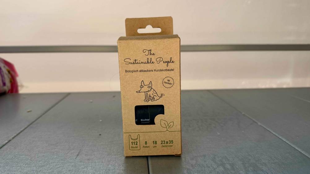 Die Verpackung der getesteten biologisch abbaubaren Hundekotbeutel steht auf einer grauen Fläche mit 112 Beutel darin.