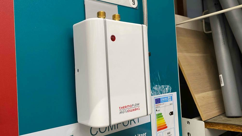 Im Test: Ein ThermoFlow Mini-Durchlauferhitzer ist an einer blauen Wand monitert.