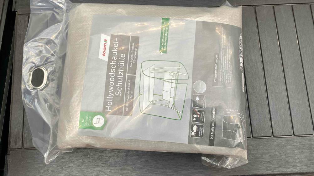 Eine getestete Schützhülle für eine Hollywoodschaukel liegt auf einer grauen Fläche in der Verpackung.
