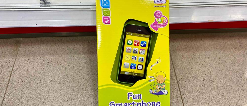 Smartphone-für-Kinder im Test: Gelbe Verpackung eines Kindersmartphones ist an einem Regal angelehnt.
