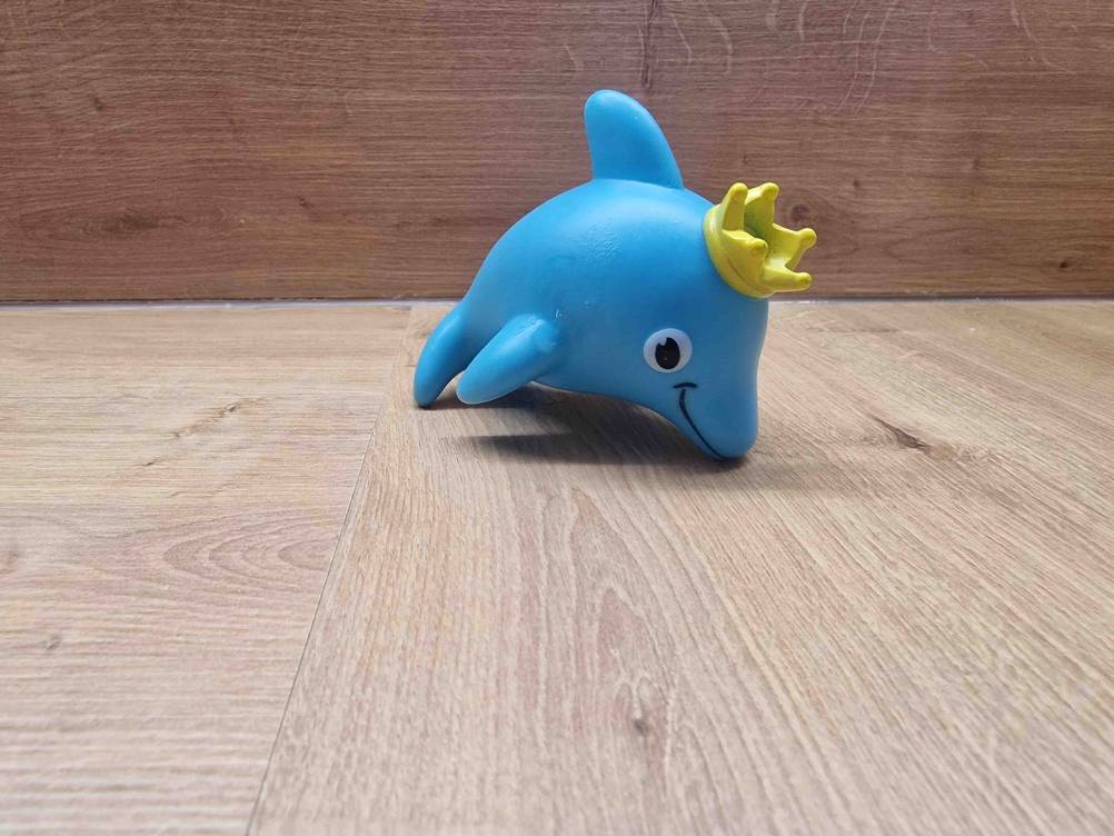 Wasserspielzeug getestet: Ein blauer Delfin mit einer Krone darauf auf einer Holzfläche platziert.