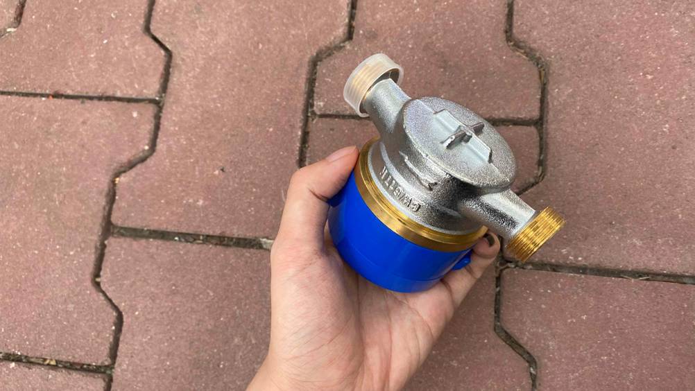Wasserzähler getestet: Eine Hand hält einen Wassserzähler vor einen Steinboden