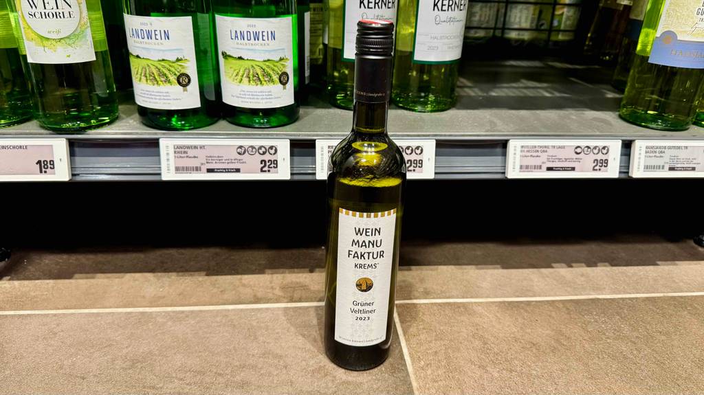 Test: Eine Flasche grüner Veltliner steht vor einem Regal worin sich ebenfalls Weinflaschen befinden.