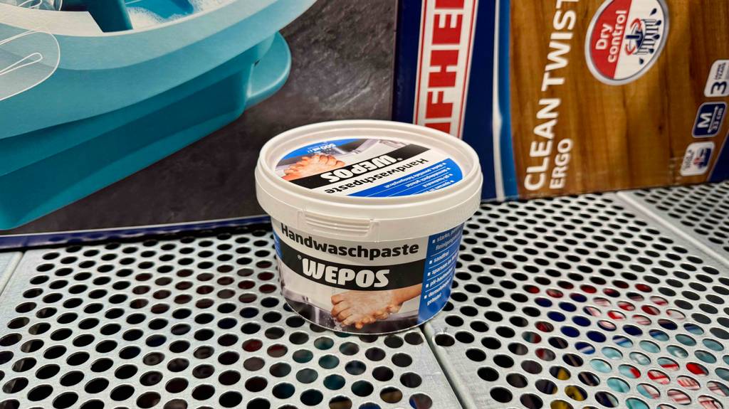 Im Test: Die Handwaschpaste im Tiegel der Marke WEPOS steht auf einem Regal mit zwei Bodenreinigungssets in ihren Verpackungen.