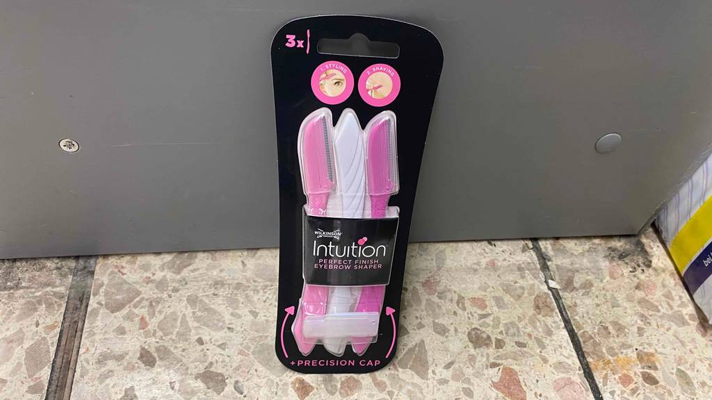 Eine Packung der getesteten Augenbrauenrasierer lehnen an einer grauen Wand