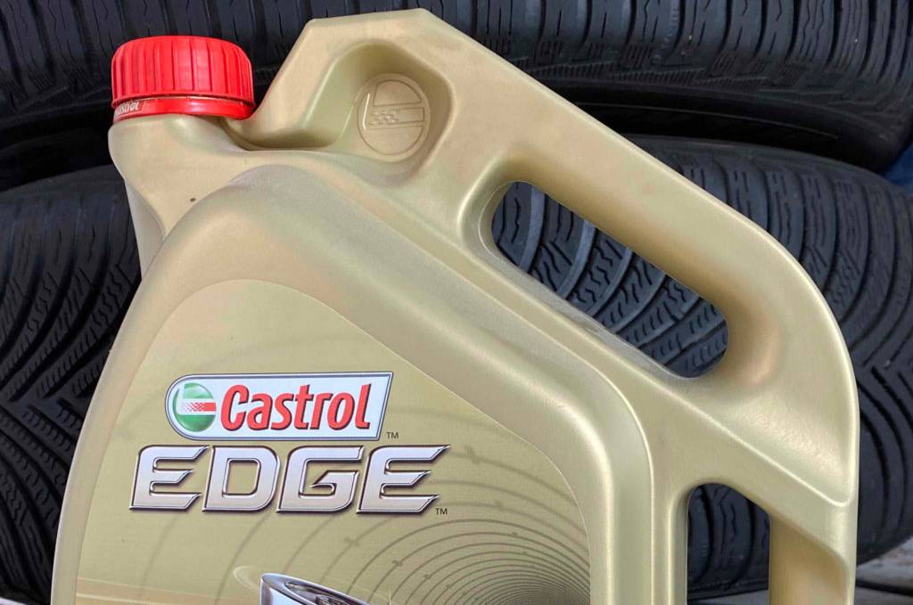 Im Test: Eine Flasche Motoröl vor Reifen auf einem grauen Boden.