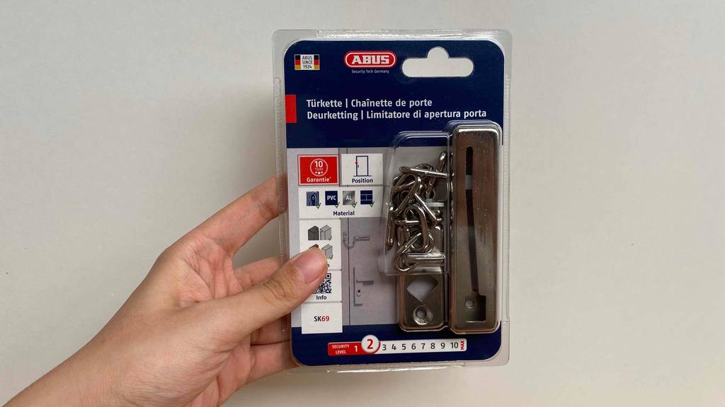 Türkette im Test: Türkette der Marke Abus wird vor einer weißen Wand in einer Verpackung gehalten.