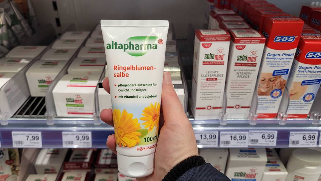 Ringelblumensalbe im Test: Ringelblumensalbe wird vor einem Regal gehalten.