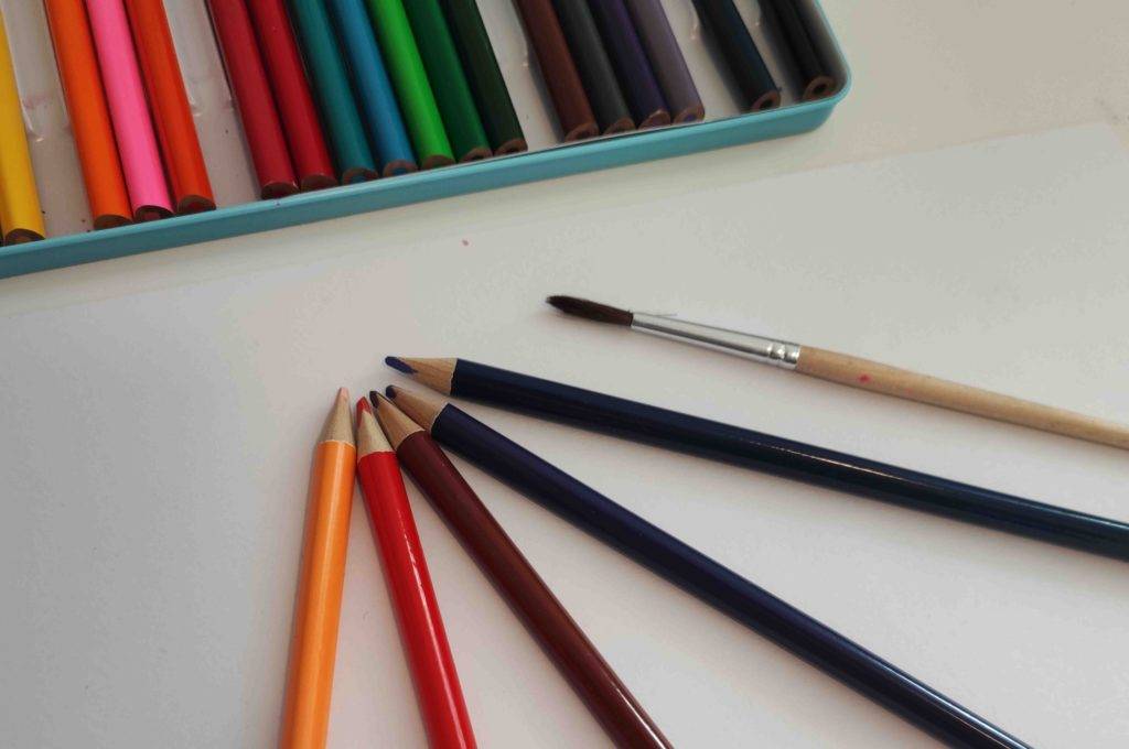 Im Test: Vor einer Box liegen vier Aquarellstifte und ein Pinsel auf einer hellen Oberlfäche.