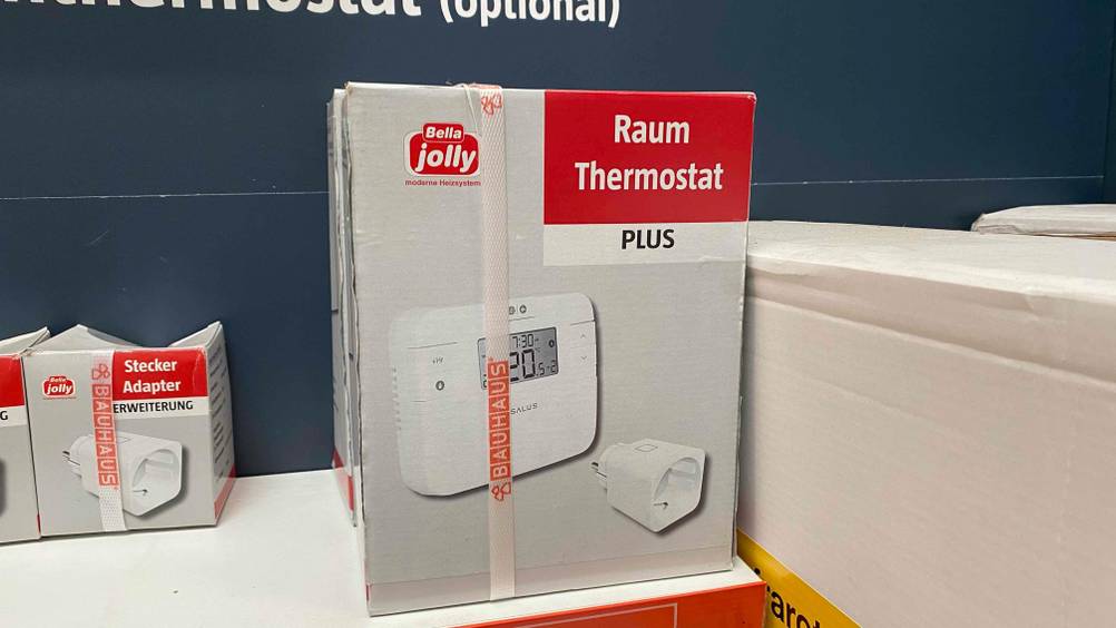 Im Test: Auf einem weißen Regal steht ein Raumthermostat neben anderen Produkten.