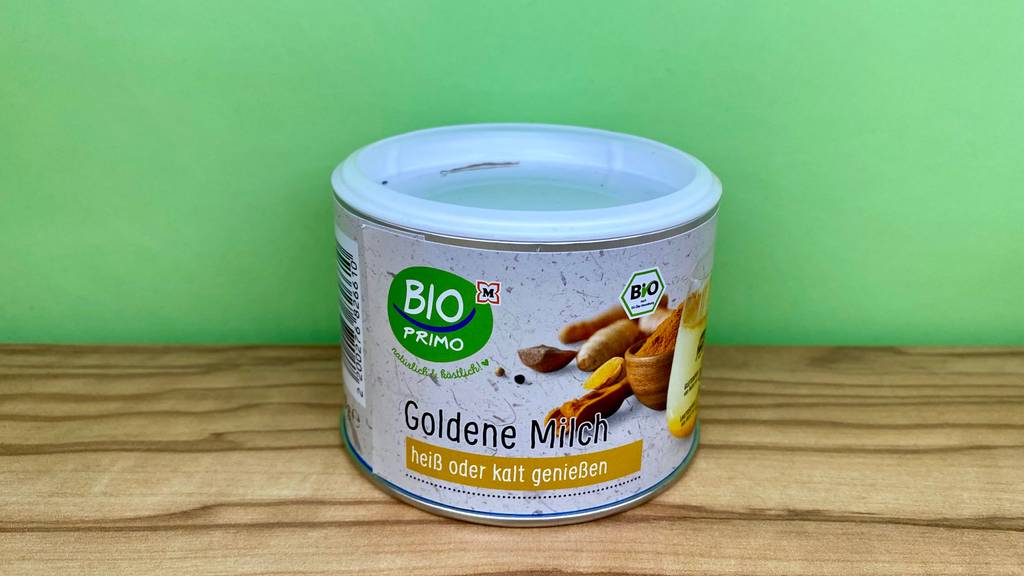 Goldene-Milch Pulver im Test: Eine Dose vor grüner Wand auf Holzoberfläche